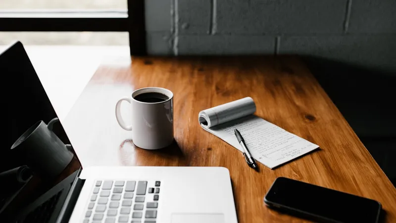 MacBook Pro laptop beside a white ceramic mug and smartphone on a minimal table